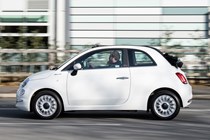 Fiat 500C (2023) review: pan shot from passenger's side, white car, wood in background