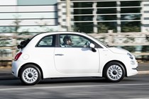 Fiat 500C (2023) review: pan shot from driver's side, white car, wood in background