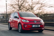 Volkswagen Up front three quarter tracking shot, red car, driving along a wooded British B-road