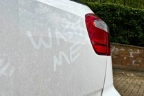 Wash me is scrawled into the dirt on a white car