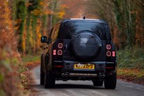 Land Rover Defender 130 V8 review: rear three quarter driving, British B-road, tree-lined, low angle, black paint