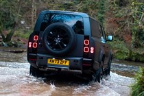 Land Rover Defender 130 V8 review: rear three quarter off-roading, fording a stream, black paint