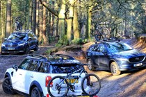 Three vehicles with bike racks shot together in a wooded area