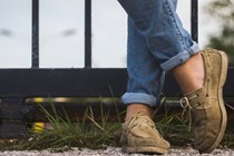 Close up of person's stone coloured deck shoes, wearing jeans and standing against railings