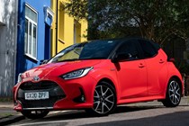 Dual-tone Toyota Yaris with red body work and black roof, shot against coloured houses of passenger side front