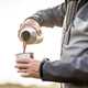 Person using a thermal flask to pour a cup of coffee outdoors