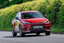 A red Lexus LBX compact SUV driving on a country road with greenery in the background. Best small luxury cars