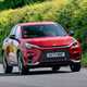 A red Lexus LBX compact SUV driving on a country road with greenery in the background. Best small luxury cars