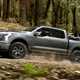 Ford F-150 Lightning electric pickup truck, side-view, driving through woods with motorbikes in loadbed