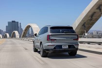 Volvo EX90 review: rear three quarter driving, grey paint, bridge in background