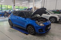 Suzuki Swift Sport (2023) long term test: front three quarter static, parked in Suzuki's workshop for its first service, bonnet up, blue car