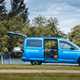 Volkswagen Caddy California campervan, side view, blue, with doors open, table, chairs, bed