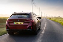 BMW i5 Touring: M60 model, rear three quarter driving, sunset, red paint