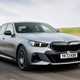 BMW 5 Series review (2024): front three quarter driving, matte grey paint