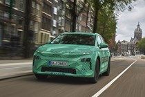 Skoda Elroq prototype: front three quarter driving, in a city, green camo wrap