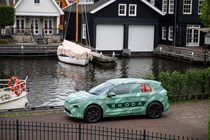 Skoda Elroq prototype: front three quarter static, green camo wrap, river and boat in background