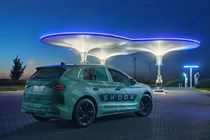 Skoda Elroq prototype: front three quarter static, green camo wrap, futuristic charging point in background