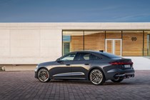 Audi A5 Sportback (2024): rear three quarter static, modern house in background, grey paint