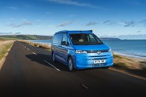 Image of a blue Volkswagen California driving along a country road, viewed from the front right corner