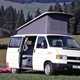 Image of Volkswagen T4 camper van in white, front right three-quarters view with raised pop-top and side door open