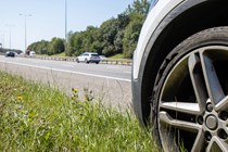 Image of a broken down car on a motorway shoulder, close-up showing the front wheel and looking down the carriageway