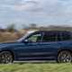 BMW X3 review (2023): passenger side pan shot, blue car, rural background