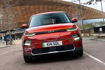 Kia Soul EV (2023): front tracking driving, orange paint, buildings in background
