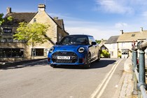 Image of a blue MINI JCW hatchback driving over a bridge, viewed from the front