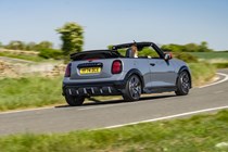 Image of a grey MINI JCW convertible driving round a corner, viewed from the rear