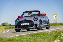 Image of a grey MINI JCW convertible driving round a corner, viewed from the front