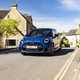 Image of a blue MINI JCW hatchback driving over a bridge, viewed from the front