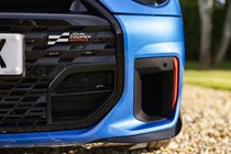 Close-up view of a MINI JCW's front left corner, showing the John Cooper Works grille badge and brake cooling duct
