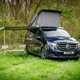 Image of the Mercedes Marco Polo parked on grass, with the pop-top raised and awning out