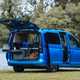 Image of a Volkswagen Caddy California parked on grass, seen from the rear right three-quarters, with tailgate open and kitchenette pulled out