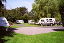 Image of a sunny campsite, with cars and caravans set up