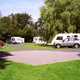 Image of a sunny campsite, with cars and caravans set up