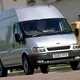 Image of a silver 2003 Ford Transit driving on an urban street, viewed from the front right corner