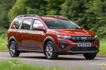 Dacia Jogger (2023) review: front three quarter driving, country lane, woods in background, orange paint