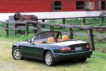 Image of a green JDM Mazda MX-5 in a horse pasture, viewed from the rear left corner