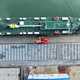 Image of a car transport ship moored at a dock, with ranks of cars waiting to be loaded