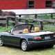 Image of a green JDM Mazda MX-5 in a horse pasture, viewed from the rear left corner