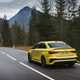Image of a yellow Audi RS3 driving through a mountain range, viewed from the rear left corner