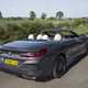 Image of a grey BMW 840d convertible with roof down, viewed while driving from the rear right corner
