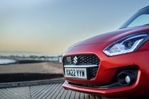 Suzuki Swift (2023) review: close-up of front end, on the beach, red paint