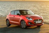 Suzuki Swift (2023) review: rear three quarter static, on the beach, red paint, sunset background