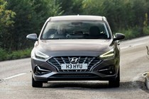 Hyundai i30 (2022) review - front cornering shot, corner entrance, brown car, leafy road