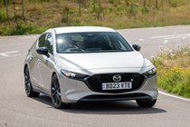 Mazda 3 (2023) review: front three quarter cornering, sharp turn showing body roll, silver paint, country lane