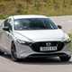 Mazda 3 (2023) review: front three quarter cornering, sharp turn showing body roll, silver paint, country lane