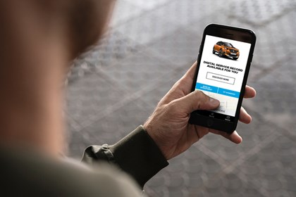 Camera looking over man's shoulder at mobile device showing Peugeot's new Digital Service History app on the screen.