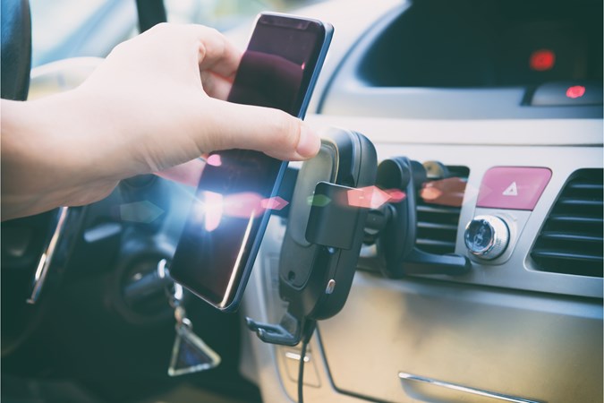 Man's hand placing smart device on in-car phone holder with wireless charging feature